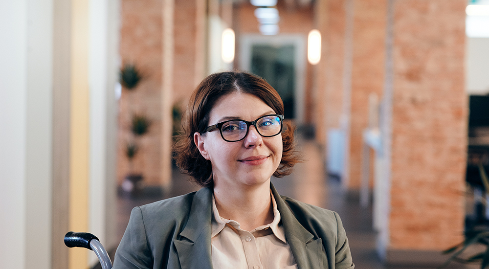 Sie sehen eine junge Frau im Rollstuhl, die über die Möglichkeiten von Barrierefreiheit in Compliance Kursen von M.I.T nachdenkt.