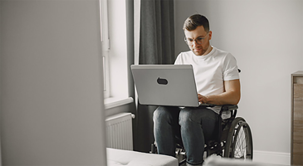 Sie sehen einen jungen mann der im Rollstuhl sitz und den neuen News Beitrag zum Thema Lernbehinderung und Assistenzsysteme auf seinem Laptop liest.