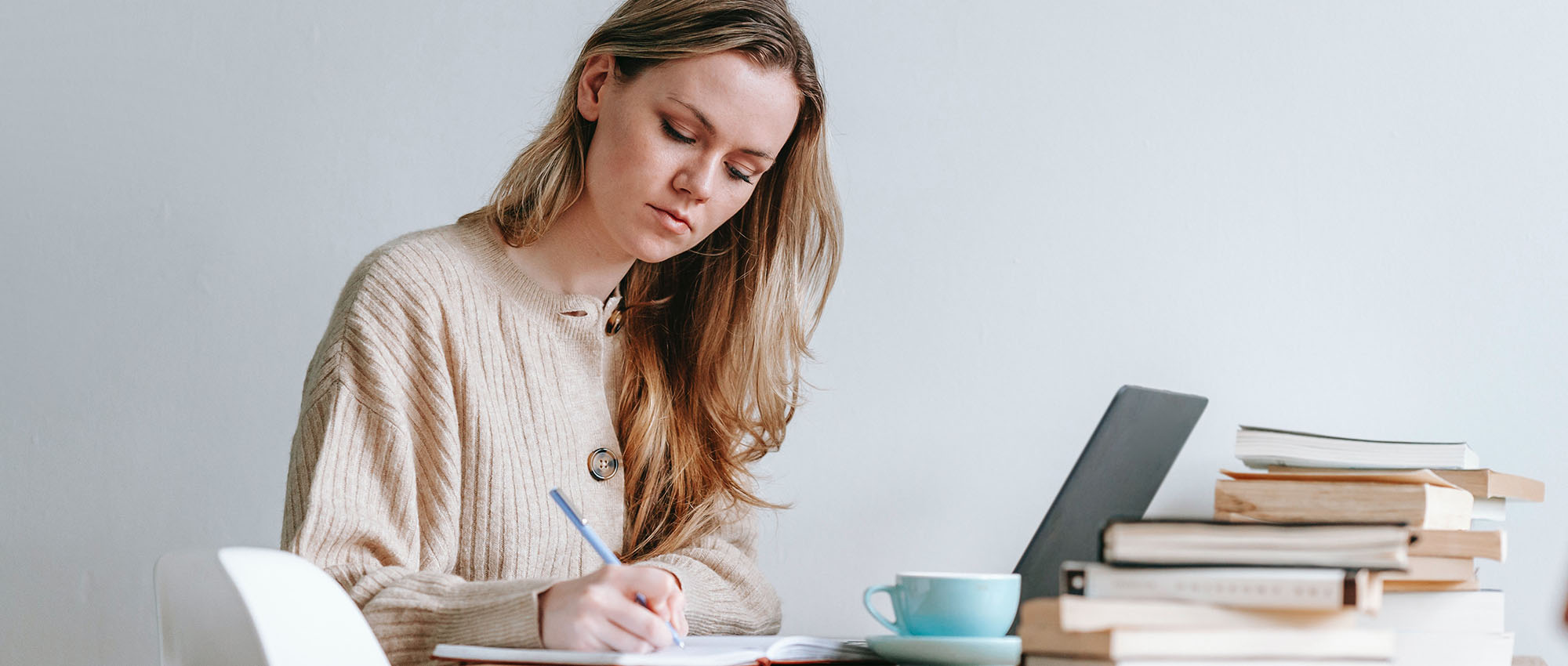 Sie sehen eine Dame an ihrem Schreibtisch die neben ihrem Laptop etwas auf einen Block schreibt. Es ist das Titelbild des Blogbeitrags "Der Nutzen von problembasiertem e-Learning".